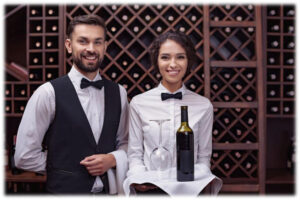 מלצרית מחזיקה מגש עם בקבוק יין וכוס יין ולצידה מלצר